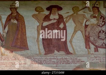 Detail aus dem 16. Jahrhundert Danza Macabra (Tanz des Todes) Freskenfries: Lächelnde Skelette stehen mit einem Papst (links), Kardinal (Mitte) und Bischof. Jeder Mann wird vom Pfeil des Todes durchbohrt und ist an seinem Kopfschmuck erkennbar: papst in päpstlicher Diadem / juwellierter dreireihiger Krone, Kardinal in Galero / breitkrempiger Hut und Bischof in Mitra. Gemalt von der italienischen Künstlerin Simone II. Baschenis (ca. 1495–1555) an der Außenwand der Chiesa di San Vigil in Pinzolo, Trentino-Südtirol, Italien. Der Fries hat Unterschriften in lokalen Dialekten und die von den gewöhnlichen Menschen verstandene Sprache. Stockfoto