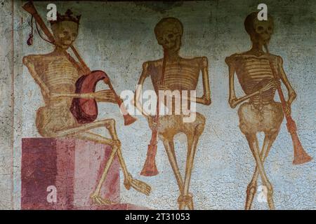 Detail aus dem 16. Jahrhundert Danza Macabra (Tanz des Todes) Freskenfries, in dem drei Skelette Musikinstrumente spielen: Gekrönter Tod (links) spielt die Dudelsackpfeifen und seine Begleiter blasen Hörner. Gemalt von der italienischen Künstlerin Simone II. Baschenis (ca. 1495–1555) an der Außenwand der Chiesa di San Vigil in Pinzolo, Trentino-Südtirol, Italien. Stockfoto