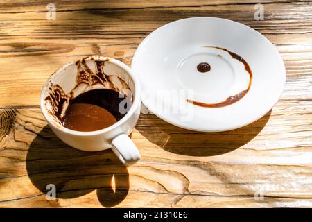 Eine Tasse türkischer Kaffee mit Mehl und Mustern, die nach dem Trinken übrig geblieben sind, und eine Untertasse, nachdem sie die Untertasse umgedreht hat, um das Glück auf dem Holztisch in St. Stockfoto