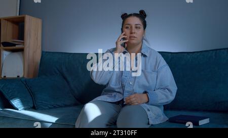 Eine Frau, die Haushaltsarbeiten erledigt. Medien. Eine wunderschöne Frau in Jeans mit wunderschöner Frisur, die auf der Couch sitzt und ein Tagebuch und ein Telefon hat. Stockfoto