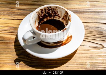 Eine Tasse türkischer Kaffee mit Mehl und Mustern, die nach dem Trinken auf der Untertasse hinterlassen wurden, nachdem man die Tasse für Glückssagen auf dem Holztisch im Straßencafe gedreht hatte Stockfoto