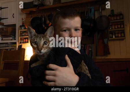 7-jähriger Junge, der seine Hauskatze (eine exotische Savannah-Rasse) in seinem Zuhause in Großbritannien hält. Stockfoto