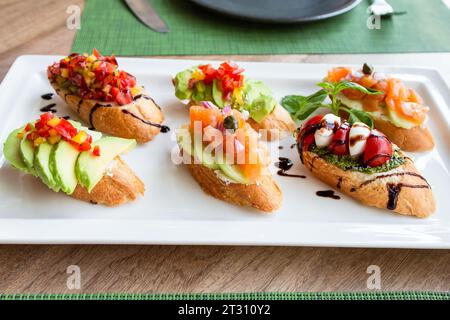 Verschiedene Bruschetta mit Vorspeisen auf weißem Teller auf Holztisch Stockfoto