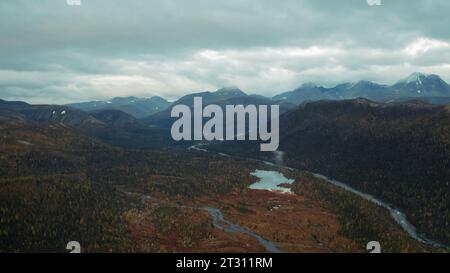 Luftflug über einen fantastischen kleinen See, umgeben von bewaldeten Tälern und Bergen. Clip. Unberührte Natur von oben am Spätherbsttag. Stockfoto