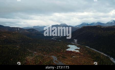 Luftflug über einen fantastischen kleinen See, umgeben von bewaldeten Tälern und Bergen. Clip. Unberührte Natur von oben am Spätherbsttag. Stockfoto