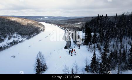 Eine filmische, epische Luftkulisse mit einer Gruppe von Skifahrern und Wanderern auf einem Berg. Clip. Winter auf dem Klippengipfel im Hintergrund des gefrorenen Flusses Stockfoto