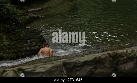 Gebirgsfluss, der im Regenwald fließt. Kreativ. Junge in einem Bach im tropischen exotischen Dschungel, Bach fließt in tiefen Wäldern zwischen Steinen. Stockfoto