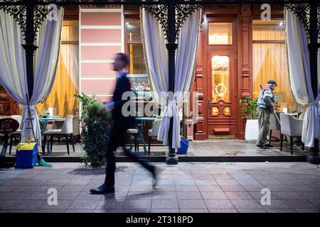 Odessa, Ukraine. Oktober 2023. Morgens geht ein Mann an einem Hotel in der Innenstadt vorbei, auf dessen Veranda ein Angestellter fegt. (Wischeffekt aufgrund langer Exposition) Credit: Sebastian Gollnow/dpa/Alamy Live News Stockfoto