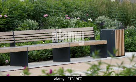 Leere Bänke im öffentlichen Park an einem Sommertag. Archivmaterial. Blühende Büsche und leere Holzbank in einem Stadtpark. Stockfoto
