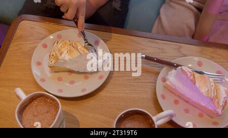 Blick von oben auf ein Mädchen, das im Restaurant Baisuekuchen isst. Archivmaterial. Genießen Sie süßen Kuchen und Kakao. Stockfoto