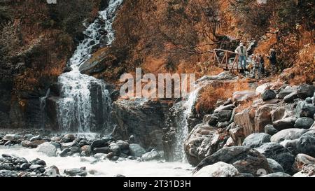 Wandern durch fabelhafte Landschaften. Kreativ. Herbstwald mit überquerenden Wasserfällen und Bäumen, in der Nähe der Menschen spazieren gehen. Stockfoto