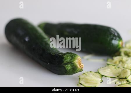 Üppige, grüne Zucchini, eine Zucchini-Spezies, die Gemüse oder auch Babymark genannt wird, fotografiert auf weißem Hintergrund zusammen mit geschredderter Zucchini. Stockfoto