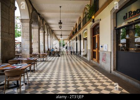 Gerona, Spanien — 31. Mai 2023. Zwei junge Leute schlendern vorbei an Restaurants im Freien am Independence Plaza, Stockfoto