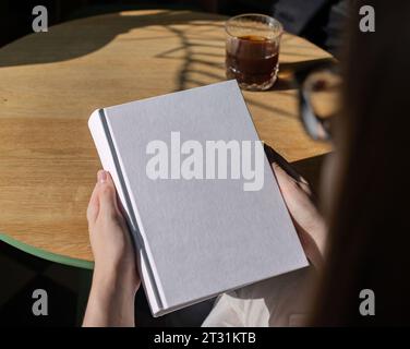 Buchcover-Mock-up, Hand hält leere, saubere Hardcover-Mockup auf Holztisch Stockfoto