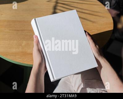 Buchcover-Mockup, Hand hält leere, saubere Hardcover-Mock auf Holztisch Stockfoto