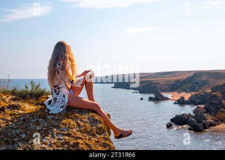 Eine Frau mit fließenden roten Haaren sitzt auf einem Berg und schaut auf die Meereslandschaft. Reisen und Tourismus. Stockfoto