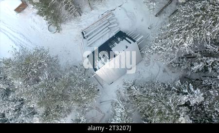 Blick von oben auf die Baustelle des Hauses im Wald im Winter. Clip. Haus im Bau in dichtem Nadelwald im Winter. Konstruktion von Stockfoto