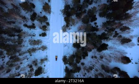 Eine Winterstraße zwischen Bäumen, die von einer Drohne genommen wurden. Clip. Winterlandschaften mit einem bewegten Mann auf einem Schneemobil in einem dunklen Wald. Stockfoto