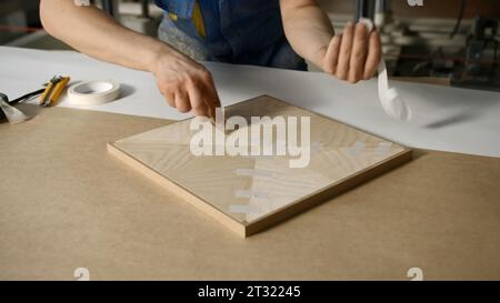 Reparaturarbeiten. Kreativ. Ein Mann in Arbeitskleidung poliert sorgfältig eine Holzfliese, um sie weiter zu überlagern. Stockfoto