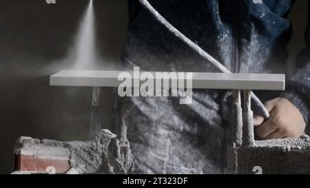 Der Mitarbeiter führt die Reparatur durch. Kreativ. Ein Mann in Arbeitskleidung und ein Locher, der eine Beschichtung mit grauer Farbe durch ein kugelsicheres Gerät macht. Stockfoto