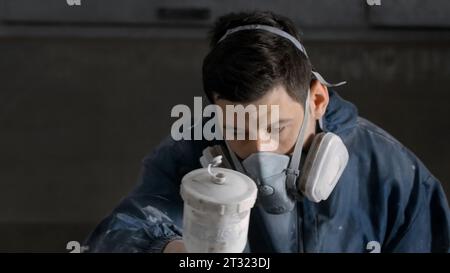 Der Mitarbeiter führt die Reparatur durch. Kreativ. Ein Mann in Arbeitskleidung und ein Locher, der eine Beschichtung mit grauer Farbe durch ein kugelsicheres Gerät macht. Hoch Stockfoto