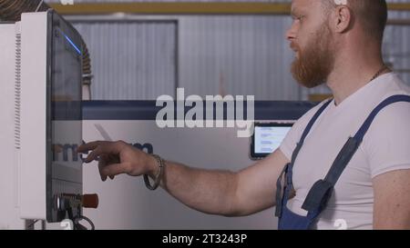 Man klickt auf das Bedienfeld der Fabrik. Kreativ. Mann in Uniform stellt die Platte im Werk ein. Bedienkonsole für Werksausrüstung Stockfoto