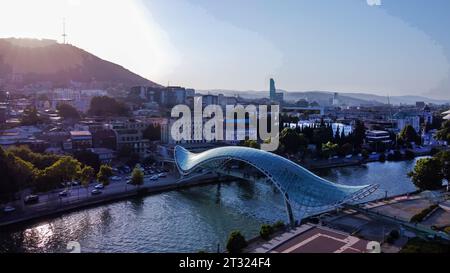 Fantastischer Drohnenblick auf die Stadtlandschaft von Tiflis mit dem Fluss Kura, der Brücke des Friedens, der Altstadt von Tiflis, dem Wolkenkratzer (Hote&) und dem Hügel W Stockfoto