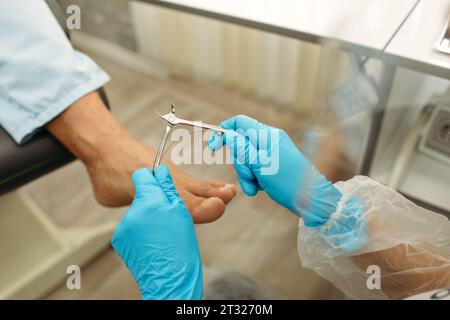 Abgeschnittenes Kopfporträt der Arztpodiatrie in blauen Handschuhen bei der medizinischen Behandlung an den Fingern im medizinischen Zentrum. Stockfoto