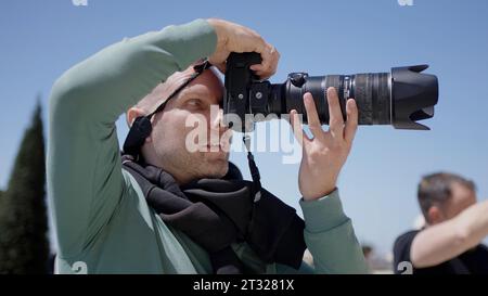 Seitenansicht eines männlichen Fotografen mit einer professionellen Kamera im Freien. Aktion. Mann, der die Kamera hält und Fotos macht. Stockfoto