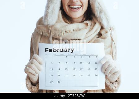 Glückliche moderne 40-jährige Frau im Wintermantel und Pelzmütze isoliert auf weiß in weißen Handschuhen mit februarkalender. Stockfoto