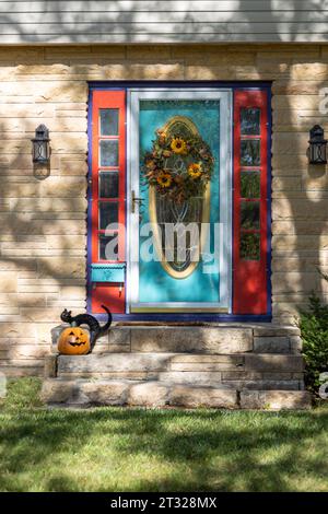 Wunderschöne aquablaue und rote Tür an einem Steinhaus mit farbenfrohen Halloween- und Herbstdekorationen Stockfoto