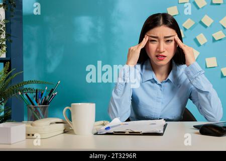 Eine von der Arbeit abgelenkte Frau fühlt sich schlecht am Computer sitzend gestresst hat einen Angstanfall am Arbeitsplatz. Gestörte weibliche Mitarbeiterin leidet im Büro an Kopfschmerzen oder Schwindel. Stockfoto