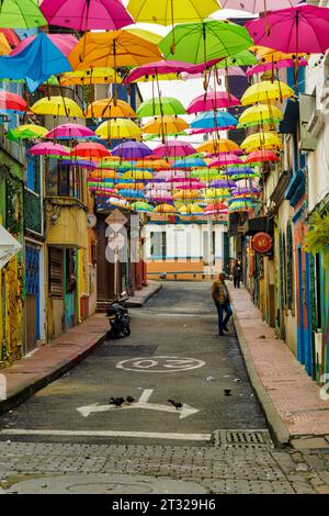 Bogota, Kolumbien - 2. Januar 2023: Touristenwanderungen durch eine mit farbigen Sonnenschirmen verzierte Gasse im Viertel La Candelaria Stockfoto