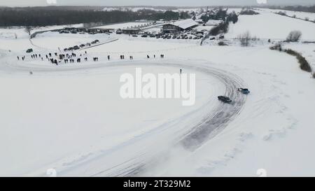 Zeitlupe einer Rennwagen-Meisterschaft, die auf einer Eisbahn gleitet. Clip. Winterliche Driftwettbewerbe, aus der Vogelperspektive. Stockfoto