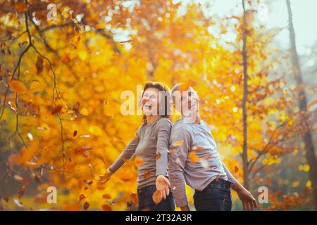 Hallo Herbst. Fröhlicher, stylischer Freund und Freundin im Park werfen Herbstblätter. Stockfoto