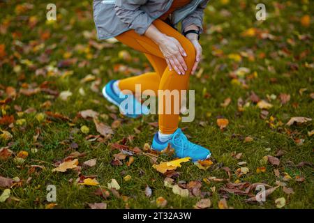 Hallo Herbst. Nahaufnahme einer Frau mittleren Alters in Fitnesskleidung im Park bekam eine Beinverletzung. Stockfoto