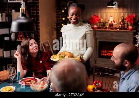 Die Familie feiert weihnachten mit festlichen Mahlzeiten und Getränken und genießt die saisonale Veranstaltung im dezember mit verschiedenen Freunden. Männer und Frauen sitzen um den Tisch, um die Wintersaison zu feiern. Stockfoto