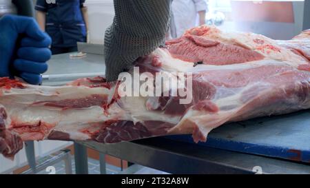 Hände eines Metzgers, der Schweinefleisch schneidet. Clip. Nahaufnahme eines Arbeiters, der Knochen vom Fleisch abschneidet, Lebensmittelindustrie. Stockfoto