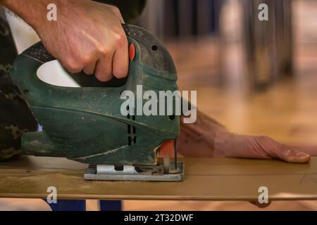 Beherrschung der Kunst der Holzarbeit: Ein erfahrener Zimmermann führt eine elektrische Stichsäge und fertigt Holzsperrholz für Möbel Stockfoto