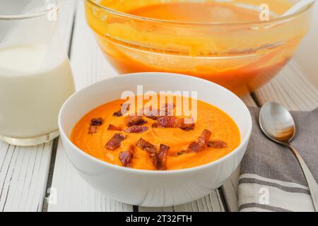 Gebratene Butternusskürbis-Suppe, serviert mit knusprigem Speck und schwerer Creme, Nahaufnahme in einer Schüssel auf einem weißen Holzbrett Stockfoto