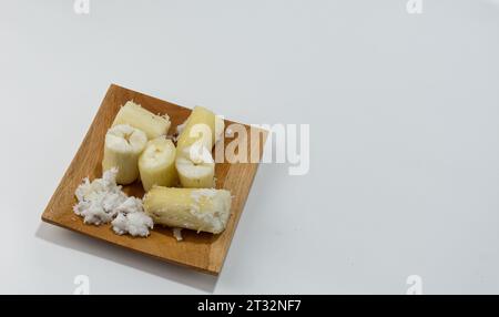 Singkong Rebus oder gekochter Maniok, begleitet von einem Streusel geriebener Kokosnuss, serviert auf einem Holzteller isoliert auf weißem Hintergrund Stockfoto