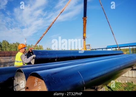 Slinger entlädt am Sommertag große Vergasungsrohre. Rohre für den Erdgastransport. Bau einer Gasleitung. Lagerung von Metallrohren mit großem Durchmesser Stockfoto