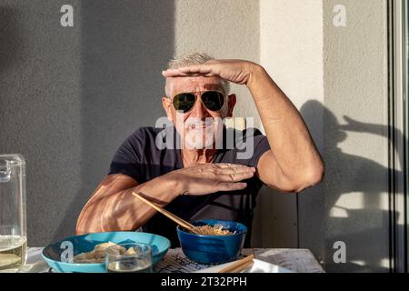 Attraktive Männer mittleren Alters haben Spaß beim Essen sitzen an einem Tisch gelegt Chinesisches Essen zum Mitnehmen vor der grauen Wand draußen Stockfoto