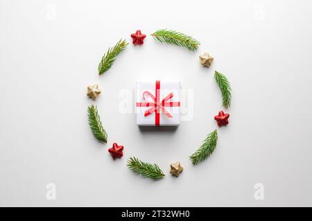 Kreativer Weihnachtshintergrund mit Weihnachtsgeschenkkasten mit rotem Band, Kugeln, Tannenzweigen und goldenen Sternen auf weißem Hintergrund. Flach, Draufsicht, Kopierraum Stockfoto