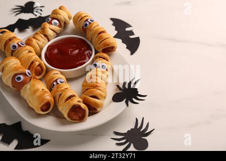 Teller mit leckeren Wurstmumien, Halloween-Deko und Ketchup auf weißem Tisch, Nahaufnahme. Leerzeichen für Text Stockfoto