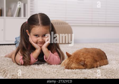 Lächelndes kleines Mädchen und niedliche Ingwerkatze auf Teppich zu Hause Stockfoto