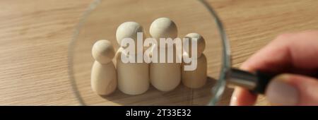 Hand einer Frau, die eine Lupe über Holzfiguren hält Stockfoto