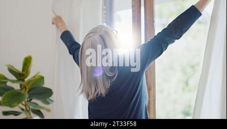 Ältere Frau zu Hause, öffnet Vorhänge und bereitet sich mit Sonne, Licht und frischer Luft auf den Tag vor. Morning Routine, Ruhestand und Senior Person bei Stockfoto