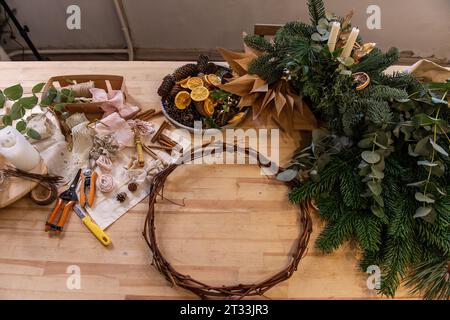 Meisterkurs, Anleitung, DIY, wie man Weihnachtskranz für den Advent macht. Auf Holztisch: Tannenzweige, Eukalyptus, Kranzbasis, Bänder, Schere, Dr Stockfoto