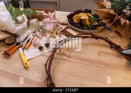 Meisterkurs, Anleitung, DIY, wie man Weihnachtskranz für den Advent macht. Auf Holztisch: Tannenzweige, Eukalyptus, Kranzbasis, Bänder, Schere, Dr Stockfoto